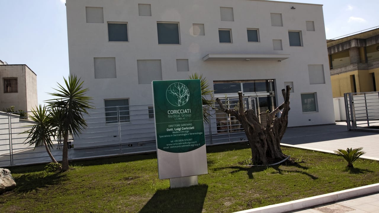 La sede di giorno: l’edificio bianco, il totem verde col nome del gruppo e del direttore sanitario, l’ulivo secolare davanti all’ingresso